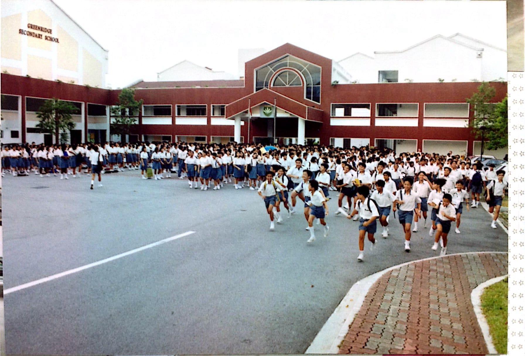 Students in white shirts and blue shorts running and gathering in the courtyard of Greenridge Secondary School.